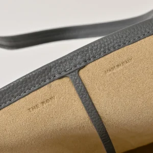 The Row bag close-up showing gray leather trim and beige suede material with embossed branding and made in Italy mark