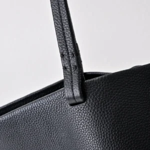 Close-up of black textured leather tote bag strap and upper edge showing fine stitching and grain detail