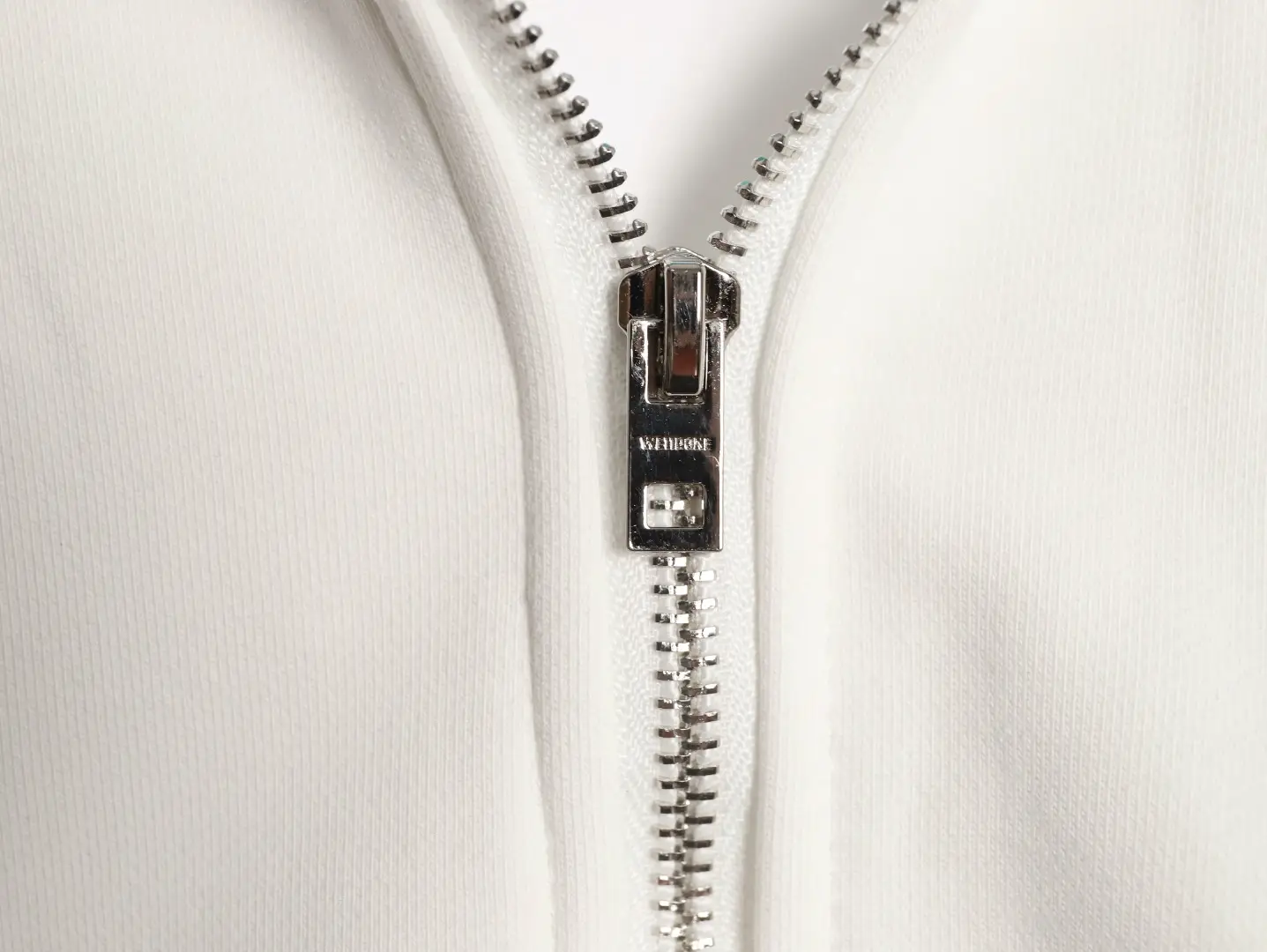 YKK silver metal zipper on white cotton fabric accessory with durable teeth and pull tab mechanism