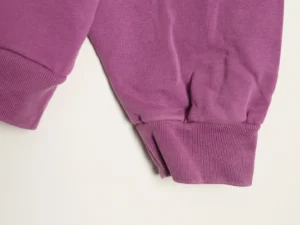 No brand or product type visible; image shows close-up of purple knit fabric with ribbed cuffs and seams.